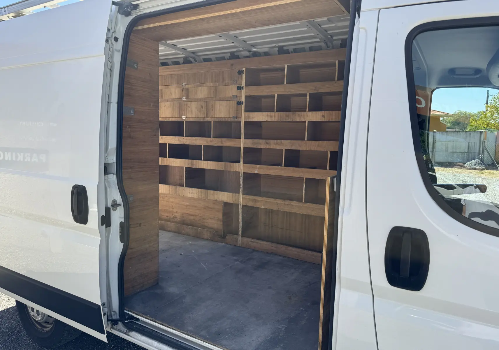 Vue latérale droite d'un Peugeot Boxer blanc 2019 avec porte coulissante ouverte, montrant l'aménagement bois intérieur du fourgon.