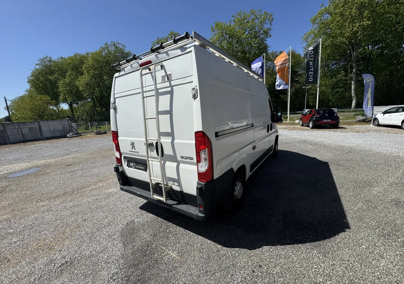 Vue 3/4 arrière droite d'un Peugeot Boxer Fourgon blanc 2019 avec échelle et galerie de toit métallique.