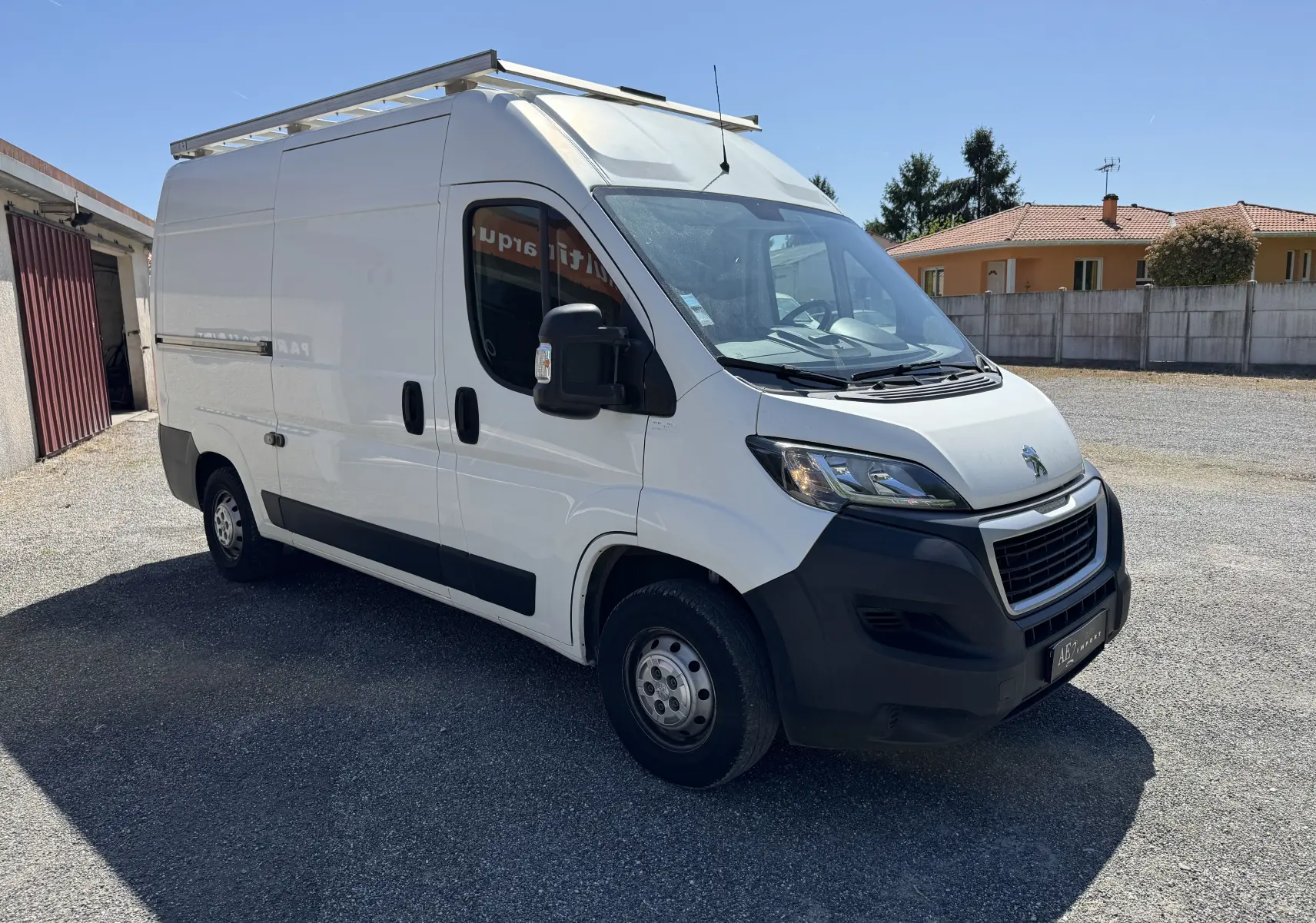 Fourgon Peugeot Boxer blanc vu en 3/4 avant droit, avec galerie de toit et pare-chocs noirs visibles.