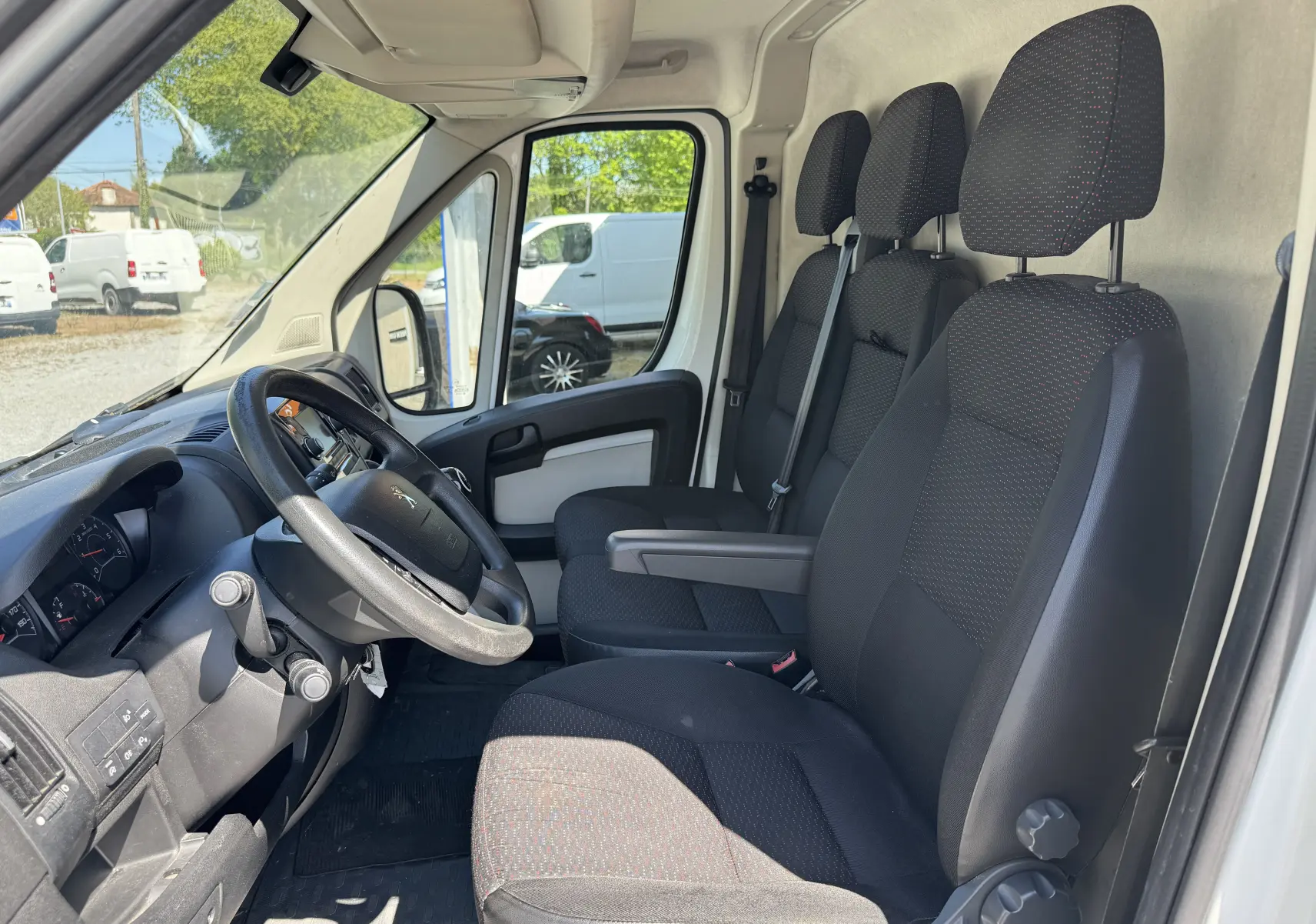 Intérieur du Peugeot Boxer Fourgon blanc 2019, vue côté conducteur montrant les sièges noirs et le volant.