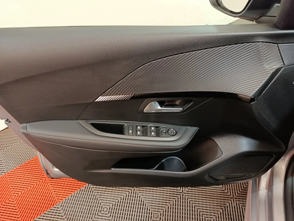 Gros plan sur la porte avant gauche gris clair de la Peugeot 208 avec commandes des vitres et insert décoratif noir texturé.