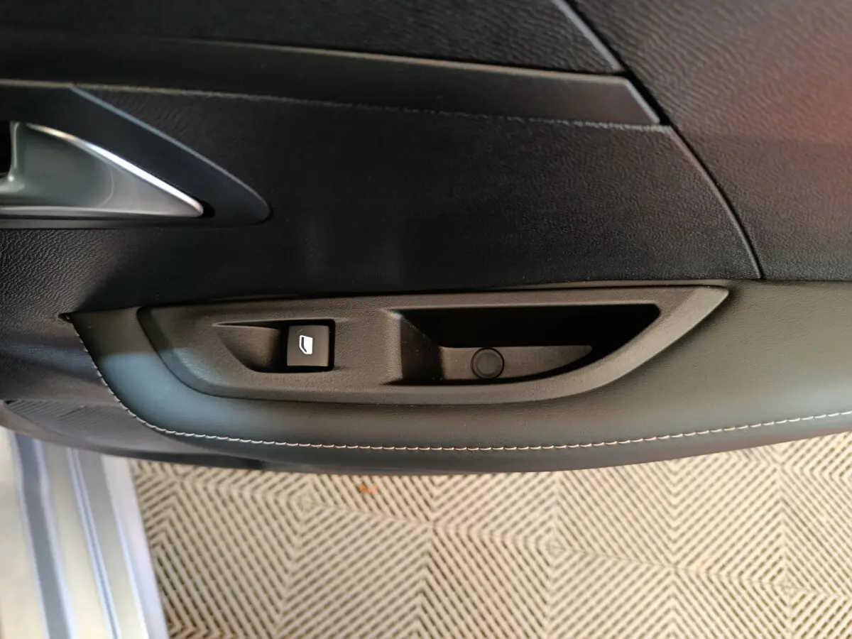 Gros plan sur la commande de lève-vitre côté gauche de la porte intérieure noire d'une Peugeot 208 gris clair.