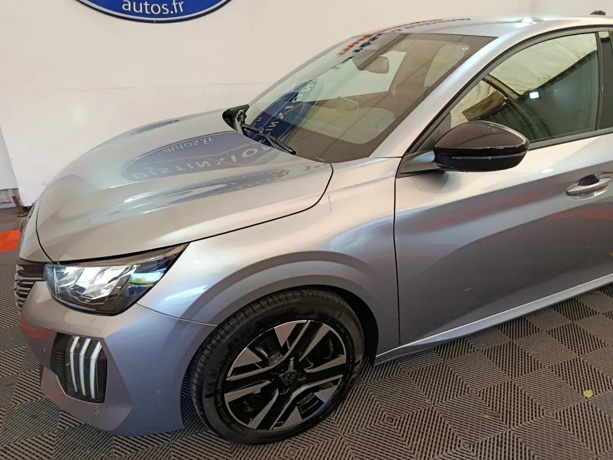 Vue 3/4 avant gauche d'une Peugeot 208 gris clair avec jantes noires et rétroviseur noir brillant.