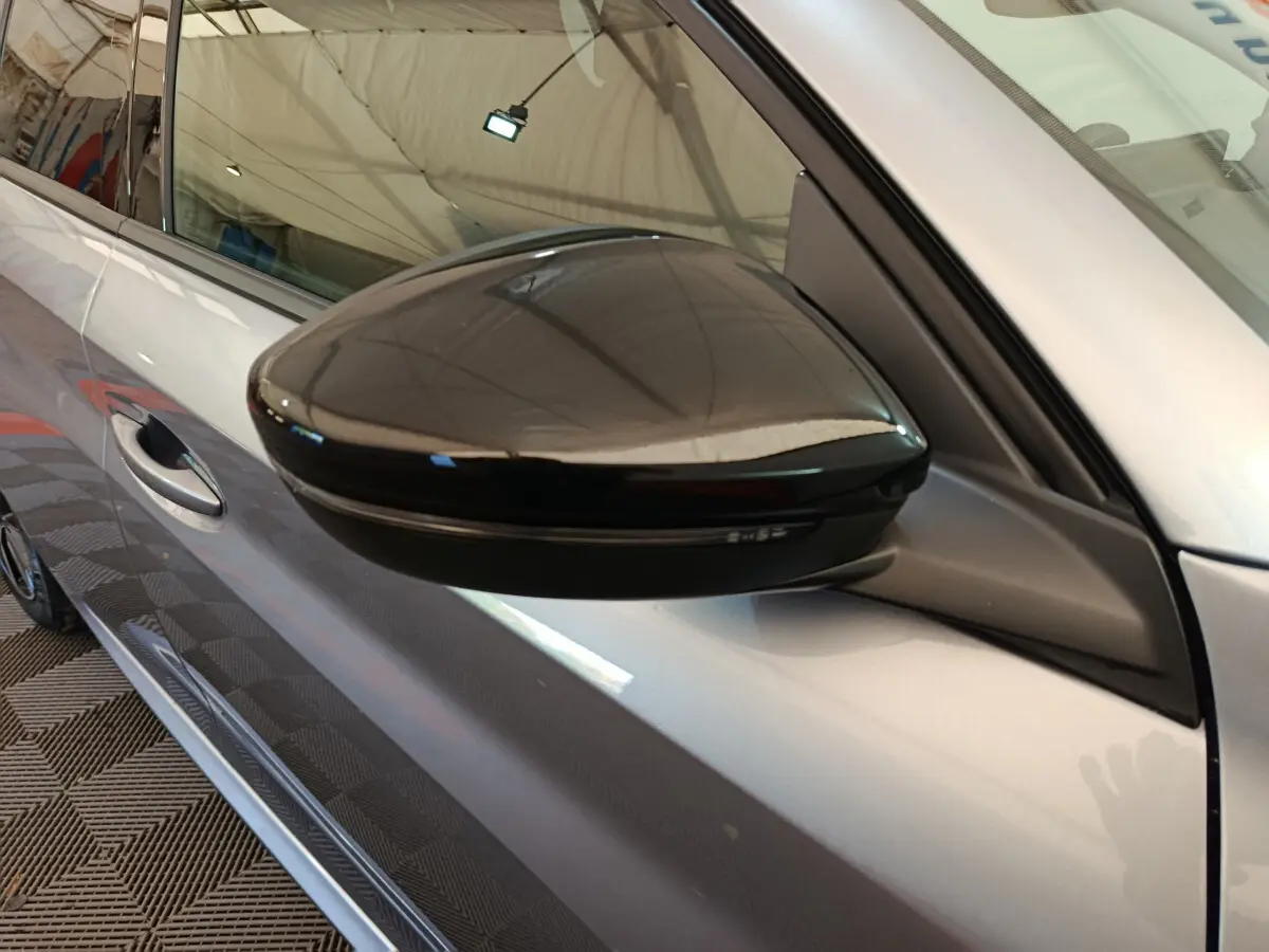 Rétroviseur noir brillant côté conducteur sur Peugeot 208 gris clair 2025, vue rapprochée du flanc avant gauche.