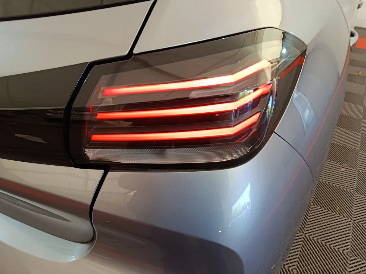 Gros plan sur le feu arrière droit allumé d'une Peugeot 208 gris clair, soulignant son design LED distinctif.