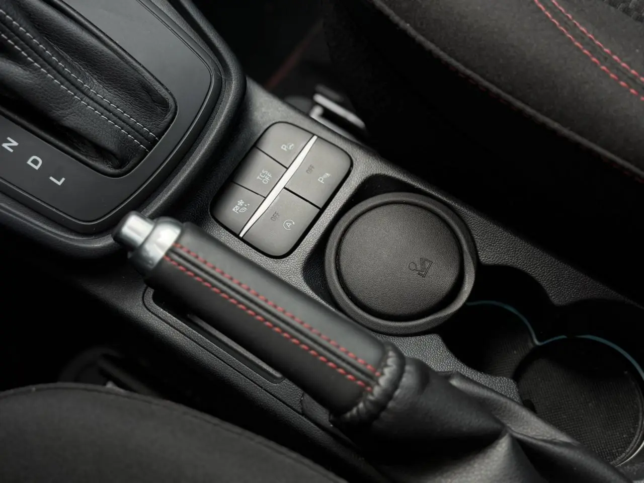 Gros plan intérieur sur le frein à main cuir noir avec surpiqûres rouges du Ford Puma Ecoboost 2024 gris magnétique.