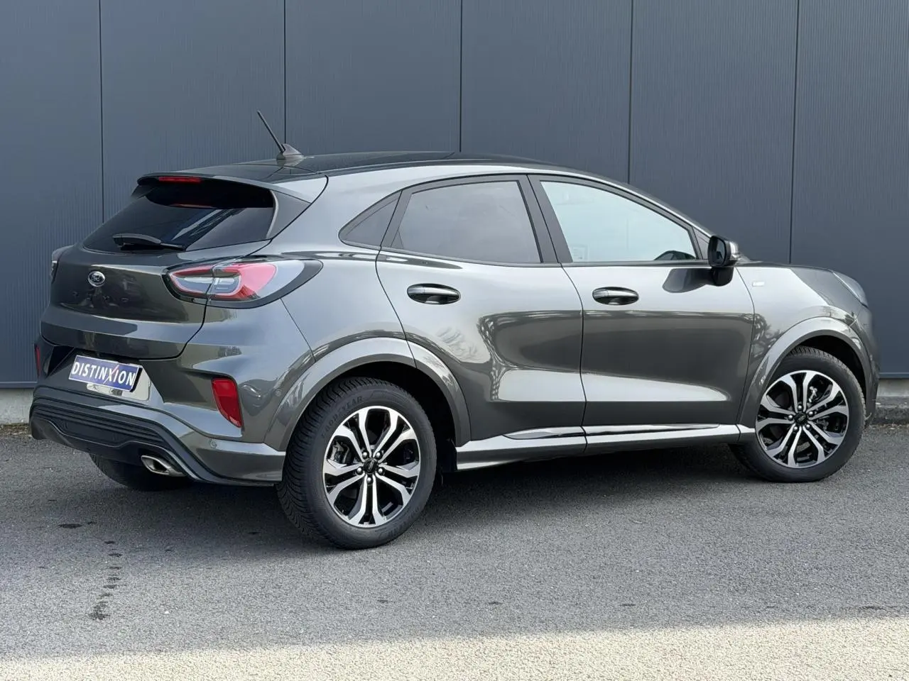 Ford Puma Ecoboost gris magnétique en 3/4 arrière droit avec jantes alliage et hayon électrique visible.