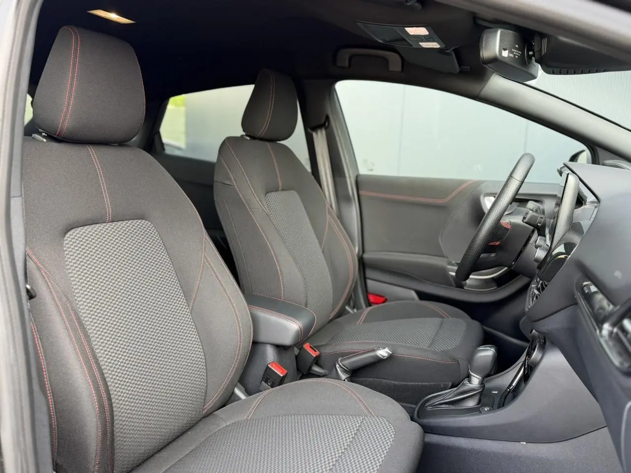 Vue intérieure côté gauche du Ford Puma 2024 Ecoboost ST Line, sièges tissu gris avec surpiqûres rouges et console centrale.