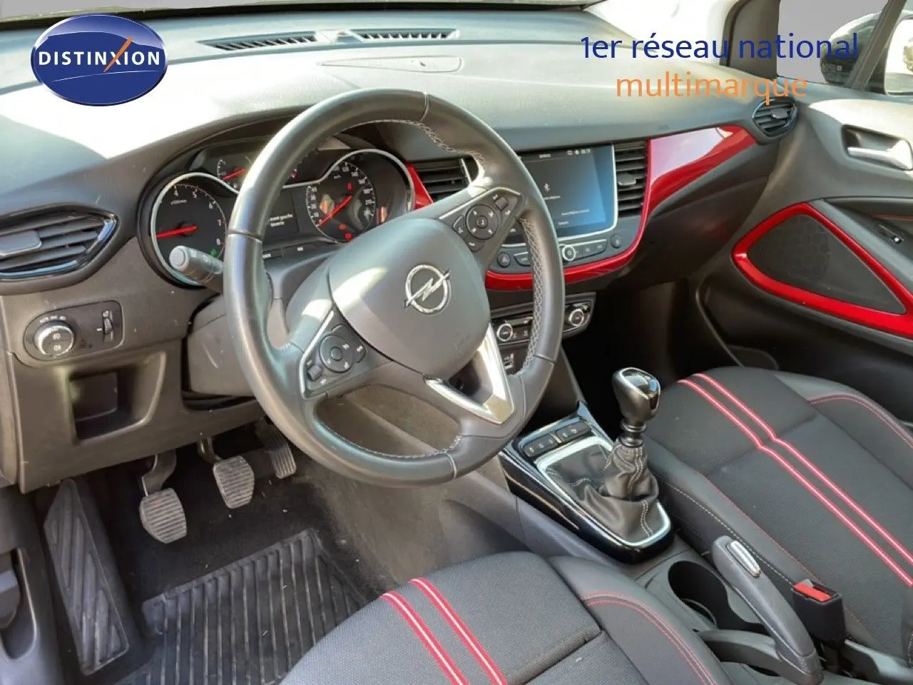Vue intérieure côté conducteur de l’Opel Crossland 2023, volant cuir, tableau de bord noir avec inserts rouges et levier de vitesse manuel.