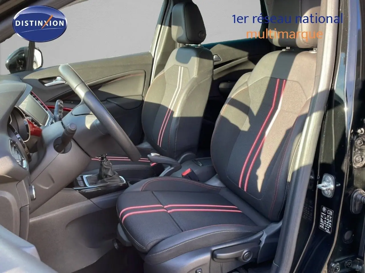 Vue intérieure côté conducteur de l’Opel Crossland noir Karbon avec sièges tissu noir à surpiqûres rouges et boîte manuelle.