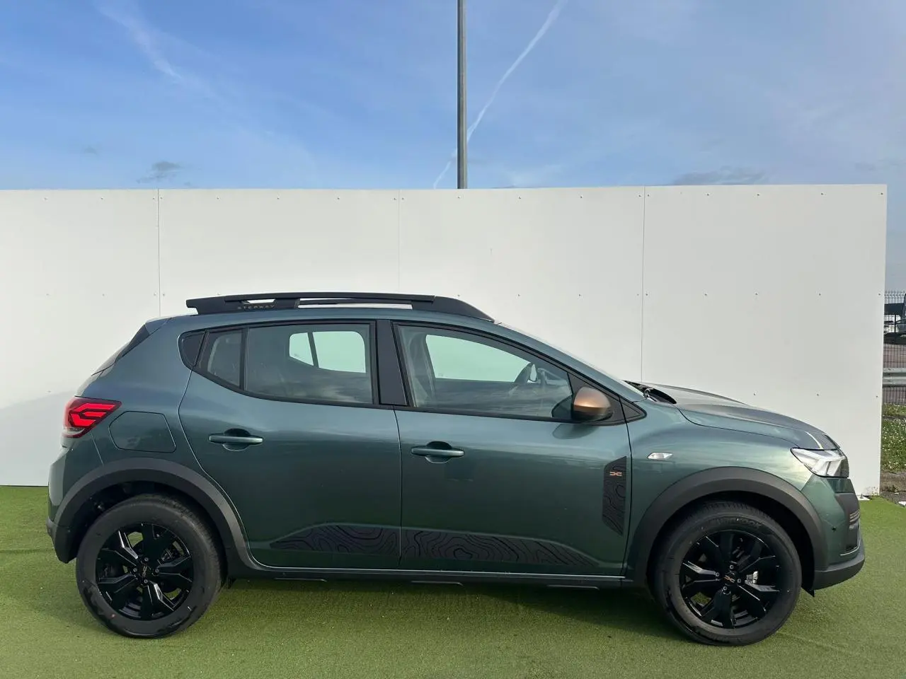 Profil droit de la Dacia Sandero Stepway 2025 en Vert Cèdre avec jantes noires et barres de toit brun cuivré.