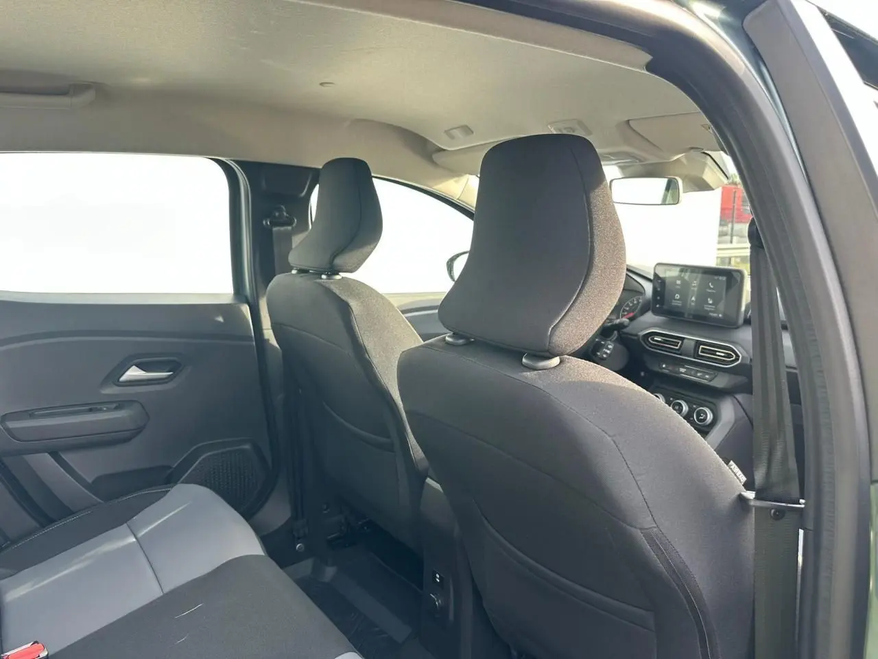 Vue intérieure arrière droite de la Dacia Sandero III Stepway, sièges noirs et tableau de bord avec écran tactile visible.