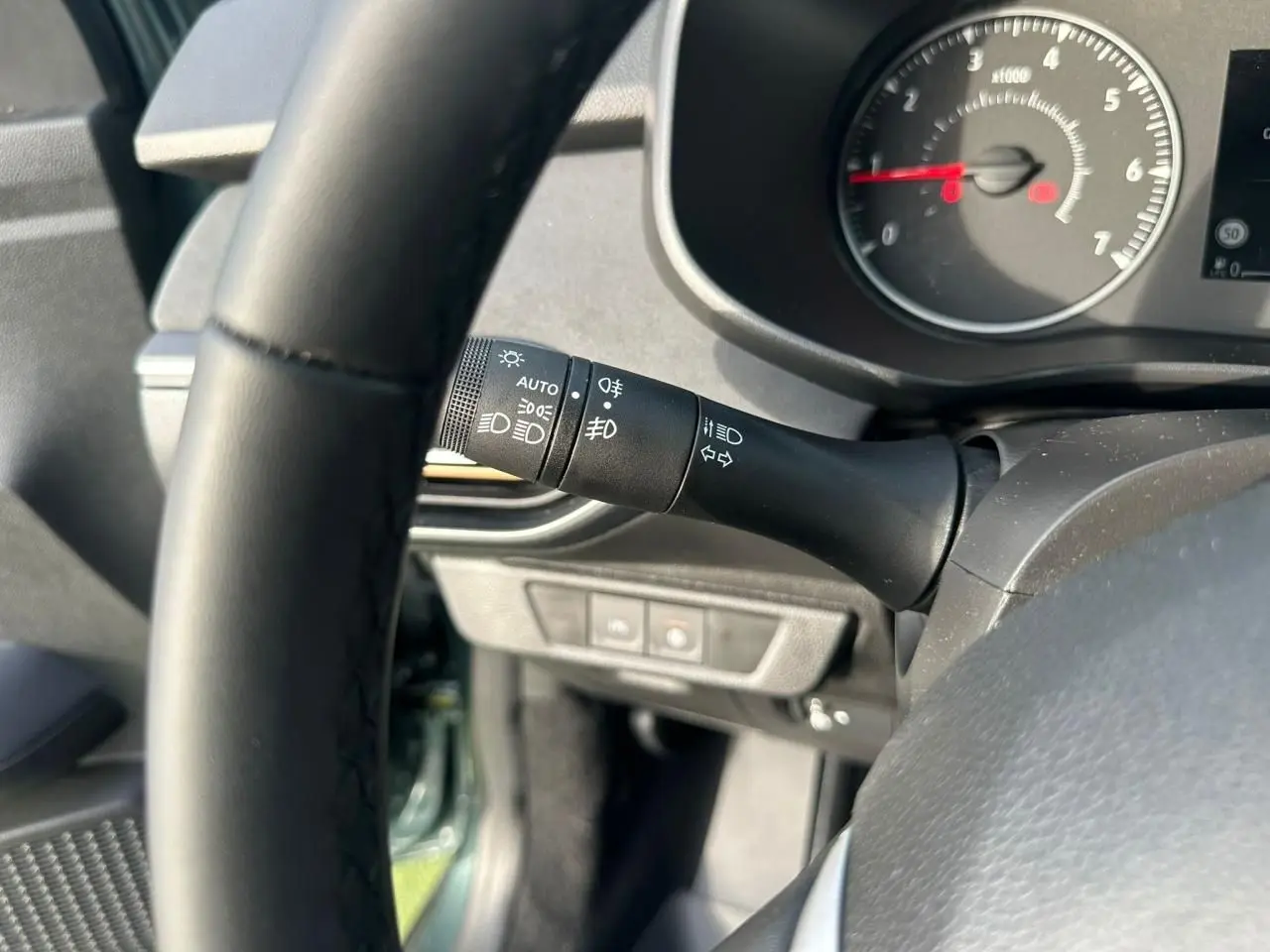 Gros plan sur la manette de commande des phares et clignotants côté gauche du volant dans l’habitacle noir du Dacia Sandero Vert Cèdre.