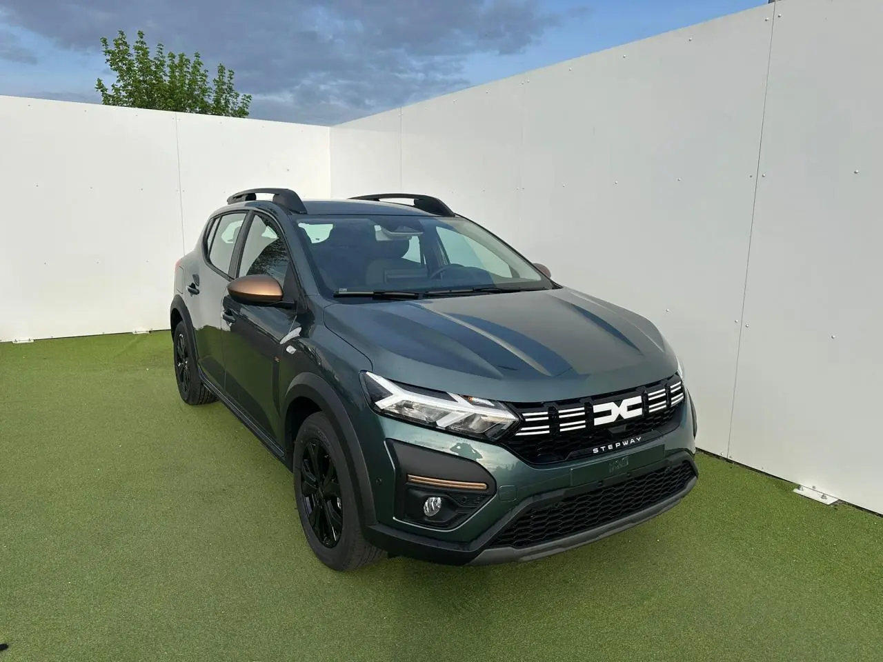 Dacia Sandero III Stepway vert cèdre en 3/4 avant droit avec calandre et rétroviseurs brun cuivré.