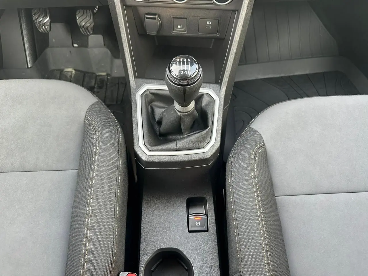 Vue rapprochée de la console centrale intérieure de la Dacia Sandero III Stepway, avec levier de vitesses manuel et frein de parking électrique.