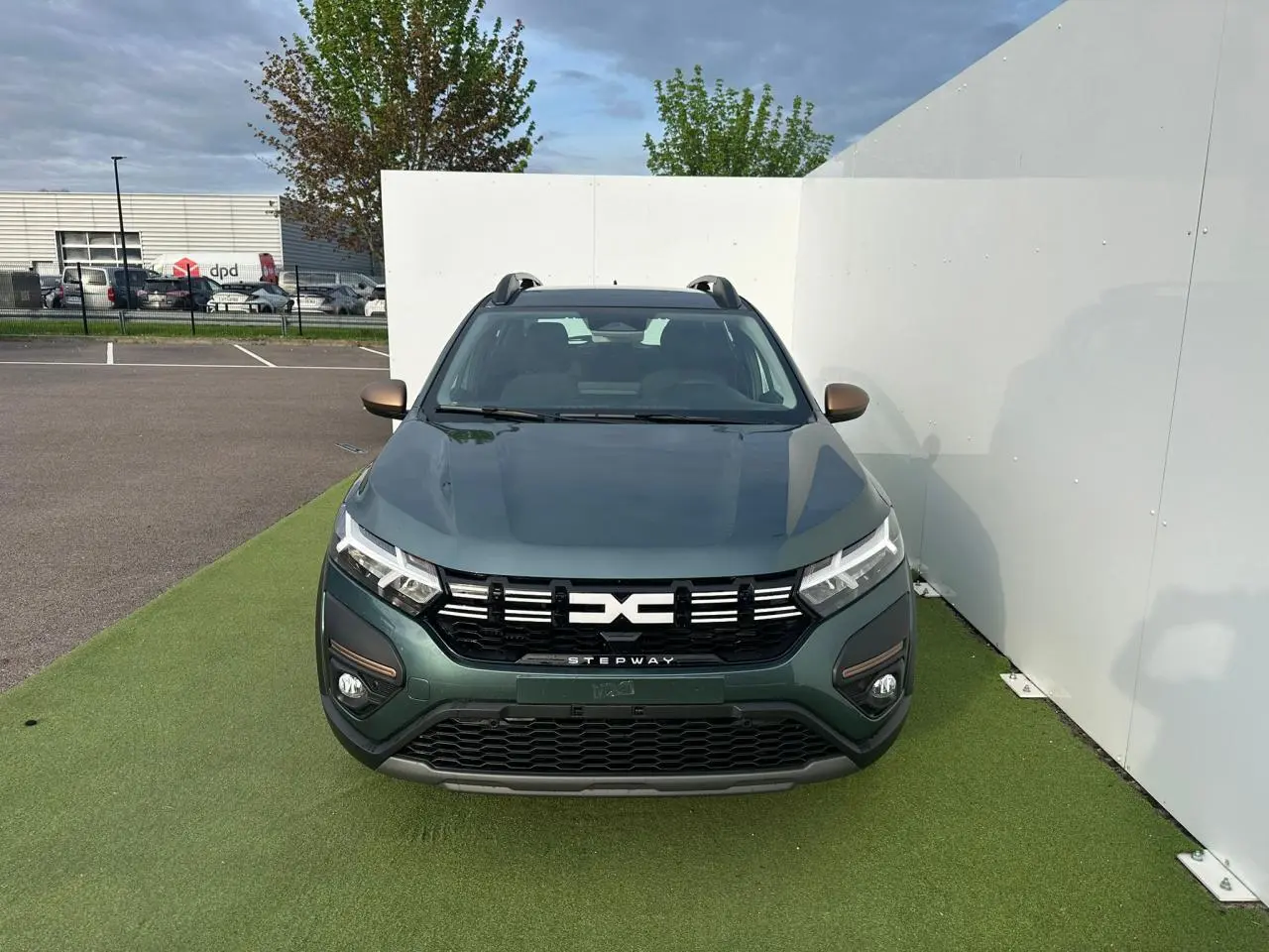 Vue avant d'une Dacia Sandero III Stepway vert cèdre avec calandre noire et barres de toit gris mégalithe.