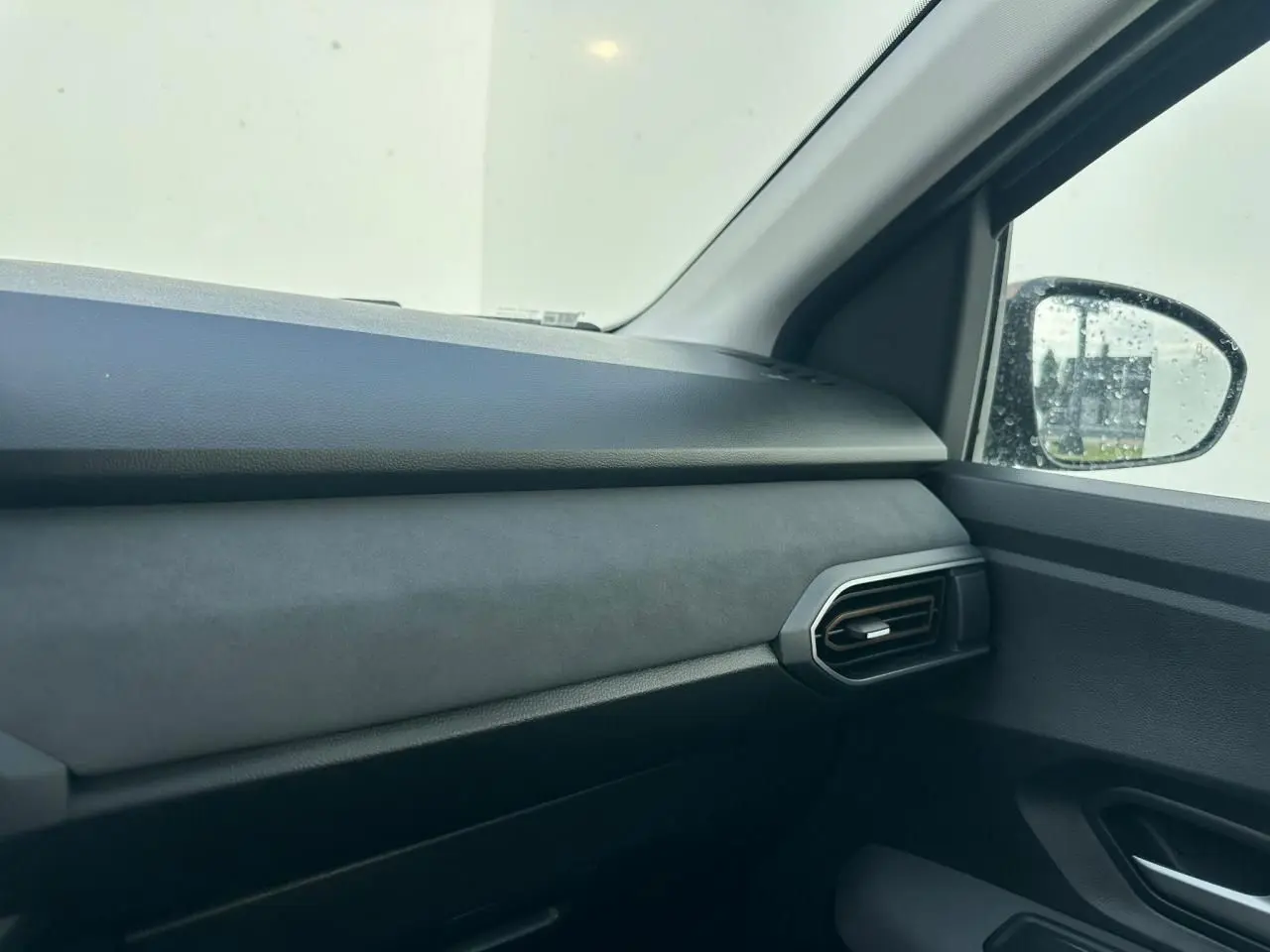 Intérieur côté passager de la Dacia Sandero III Stepway 2025, tableau de bord gris et sortie d'air hexagonale.