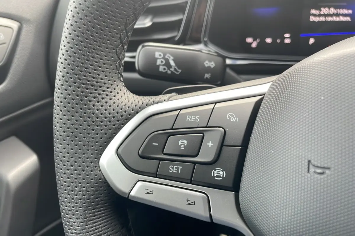 Gros plan sur le volant cuir noir perforé du Volkswagen T-Roc 2025, boutons multifonctions et commandes de régulateur visibles.