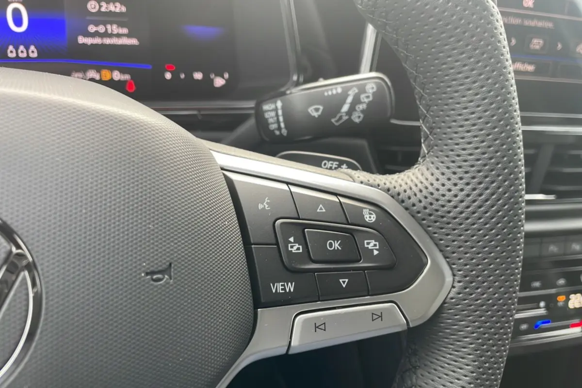 Gros plan sur le volant cuir perforé du Volkswagen T-Roc 2025 avec commandes multifonctions et affichage digital en arrière-plan.