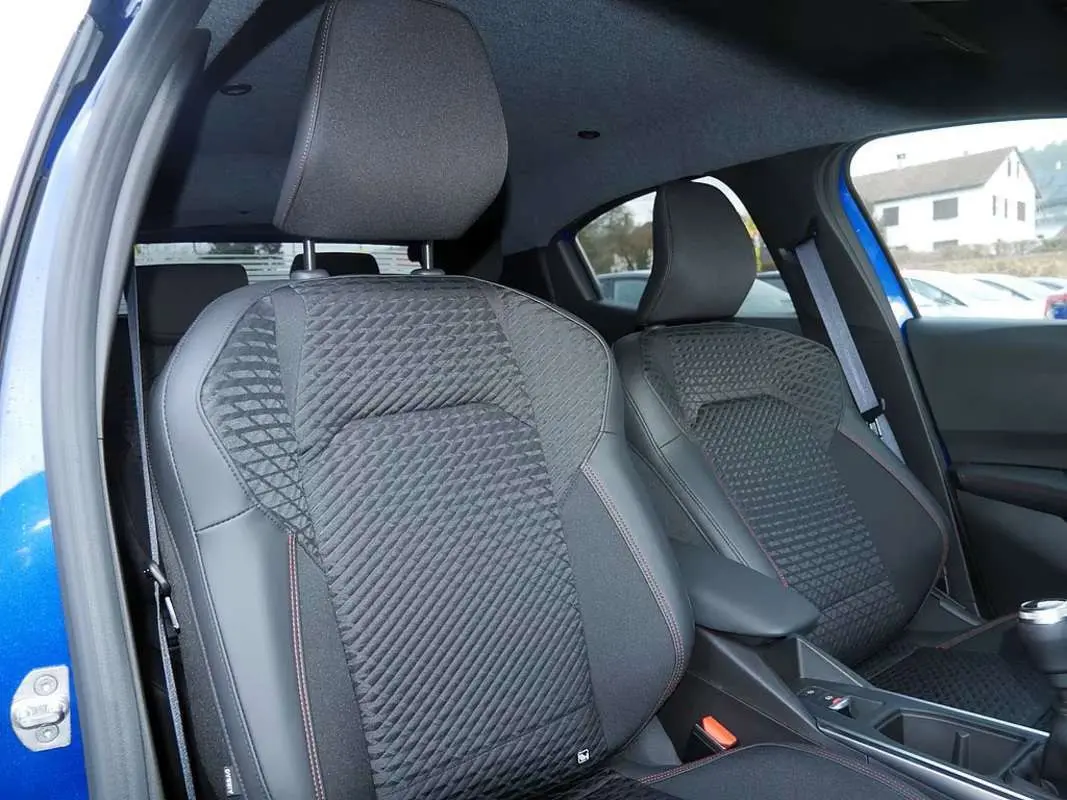 Vue intérieure rapprochée des sièges avant en tissu noir avec surpiqûres rouges d’une Renault Clio bleu iron.