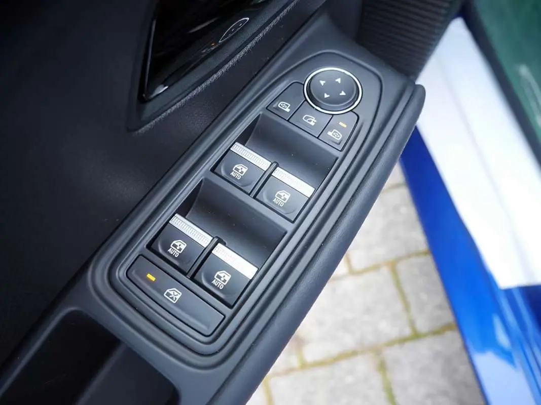 Gros plan sur les commandes des vitres électriques côté conducteur de la Renault Clio VI bleu iron, porte ouverte.