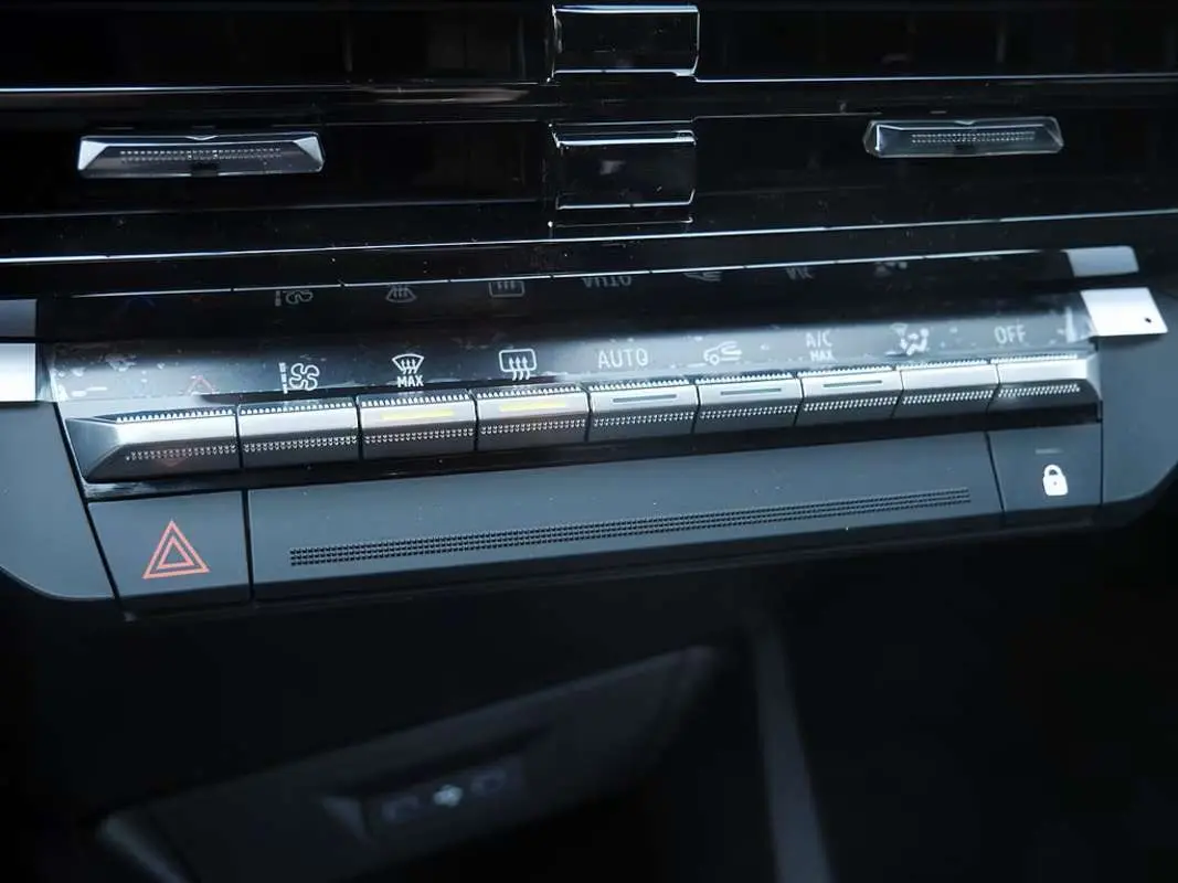 Gros plan sur la console centrale de la Renault Clio VI bleu iron, mettant en valeur les commandes de climatisation automatique et les boutons multifonctions.