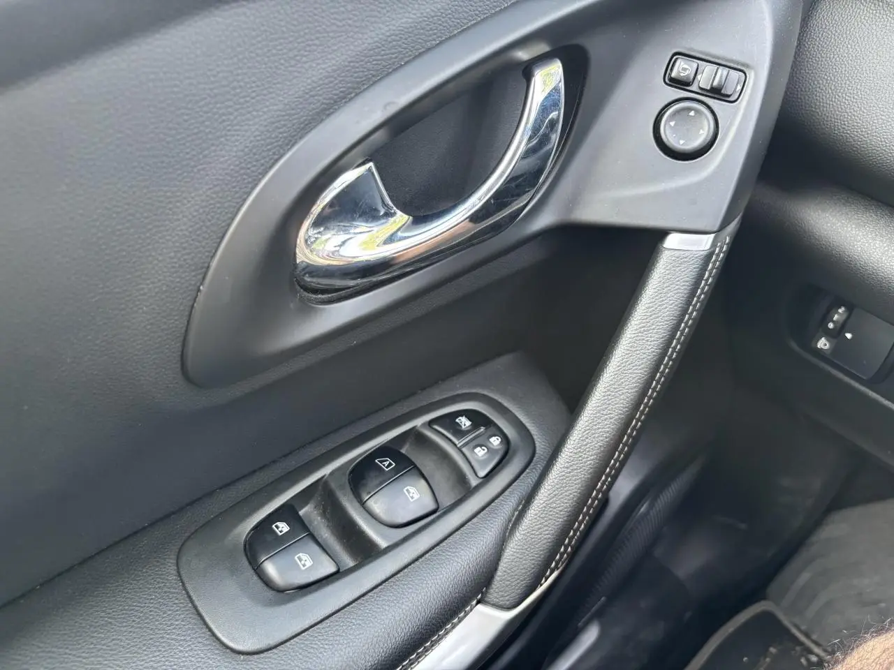 Gros plan sur la poignée de porte intérieure côté conducteur du Renault Kadjar gris foncé avec commandes électriques des vitres et rétroviseurs.