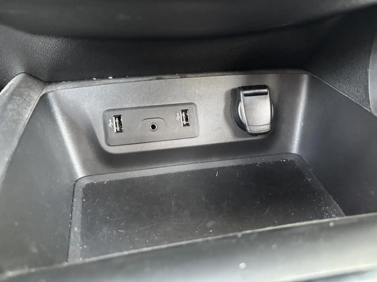 Gros plan sur la prise USB double et prise 12V dans le compartiment de rangement intérieur du Renault Kadjar gris foncé.