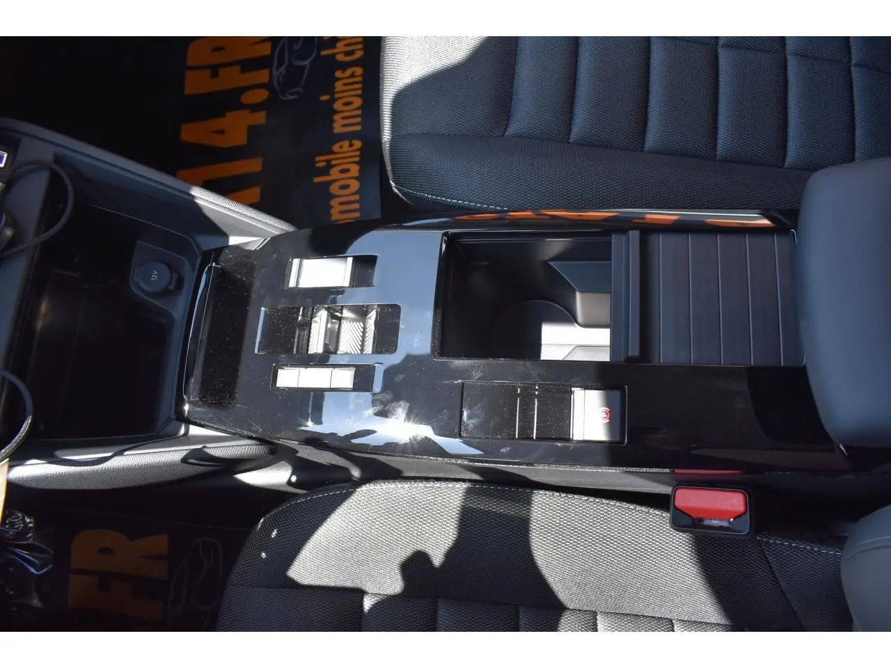 Vue plongeante sur la console centrale noire brillante de la Citroën C4 Hybride 136 e-DCS6 Plus avec sièges tissu gris.