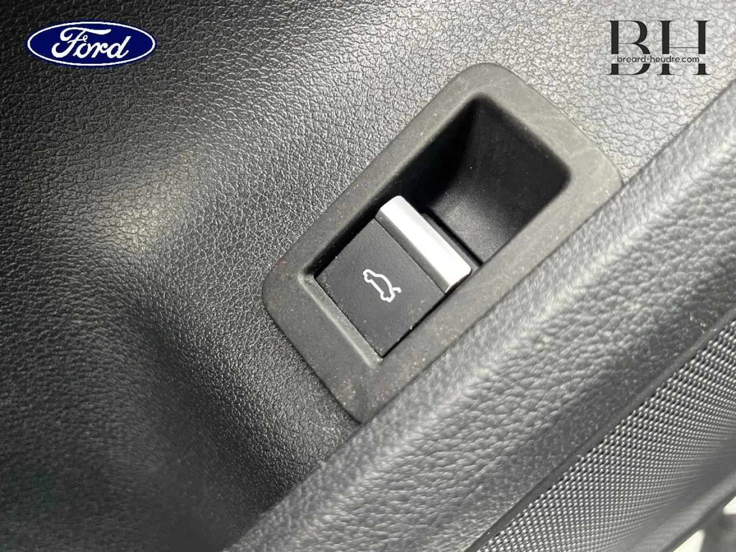 Bouton d'ouverture du coffre sur panneau intérieur noir, détail d'une Audi A4 Avant blanc glacier métallisé 2021.