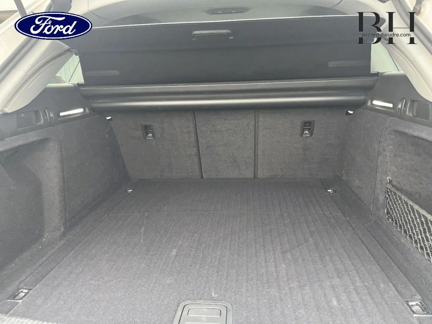 Coffre ouvert d'Audi A4 Avant blanc glacier, vue intérieure arrière montrant un espace de chargement spacieux et tapis noir.