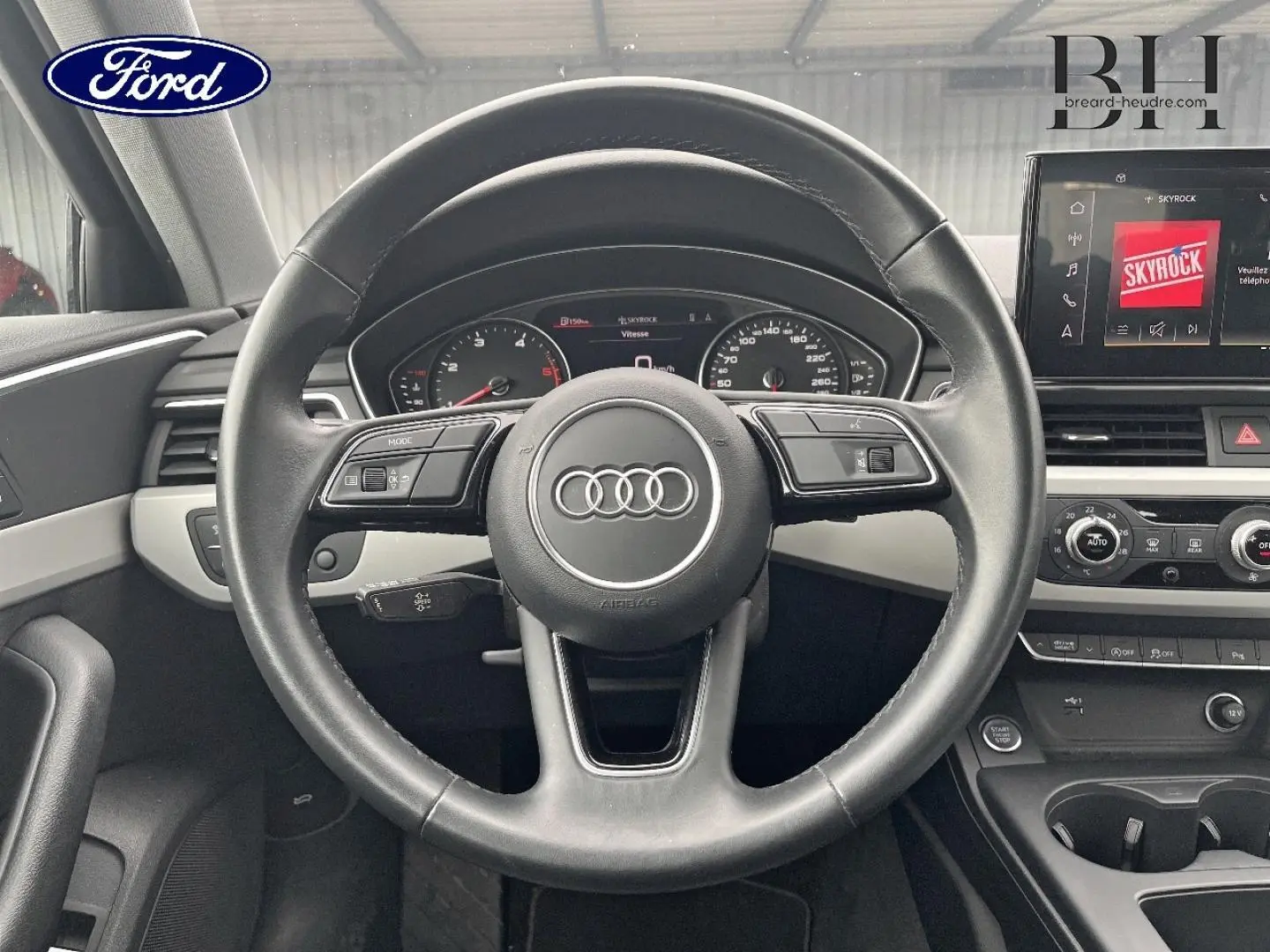 Vue intérieure centrée sur le volant cuir Audi avec tableau de bord et écran multimédia en arrière-plan.