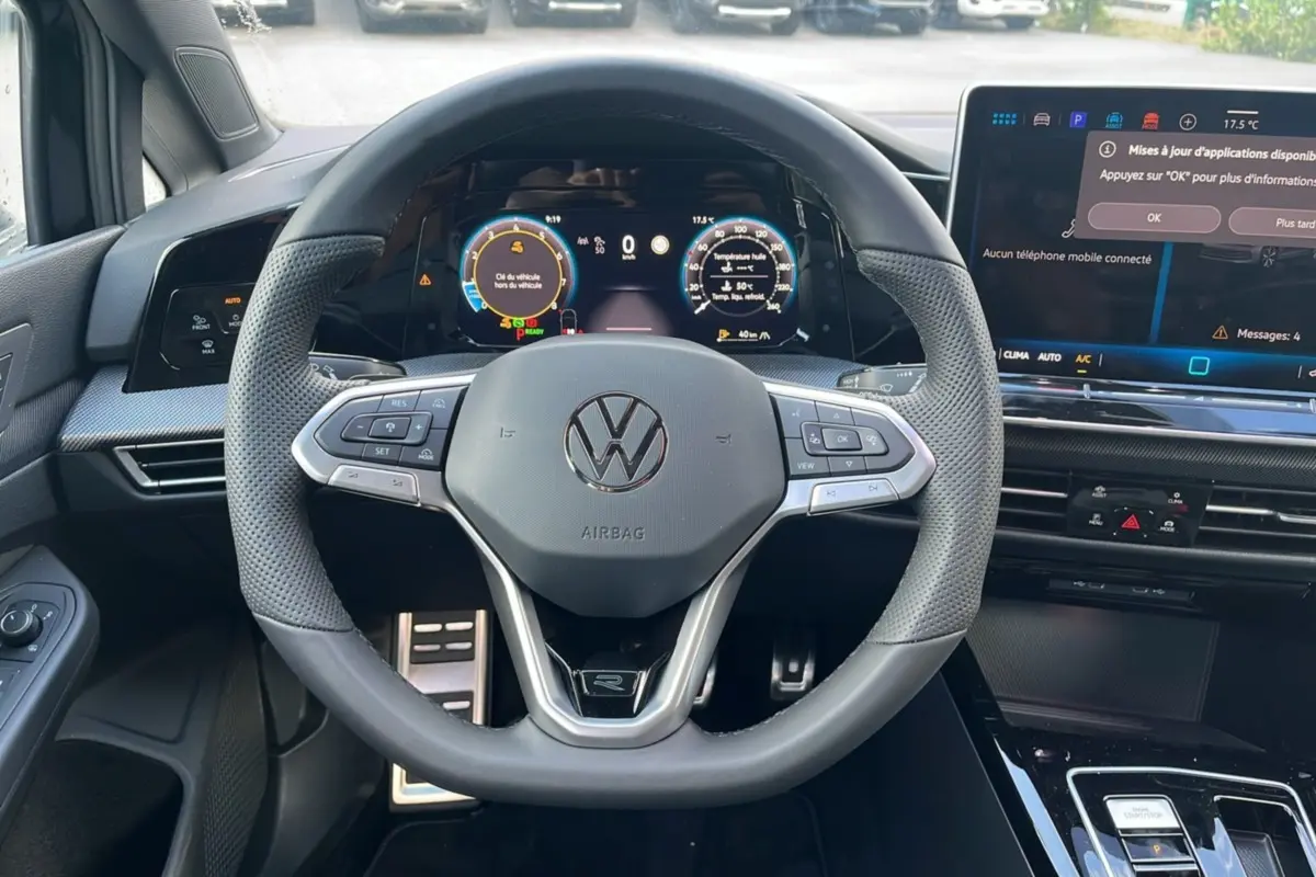 Vue intérieure centrée sur le volant cuir multifonctions R-Line de la Volkswagen Golf E-TSI 150 noire, avec tableau de bord digital.