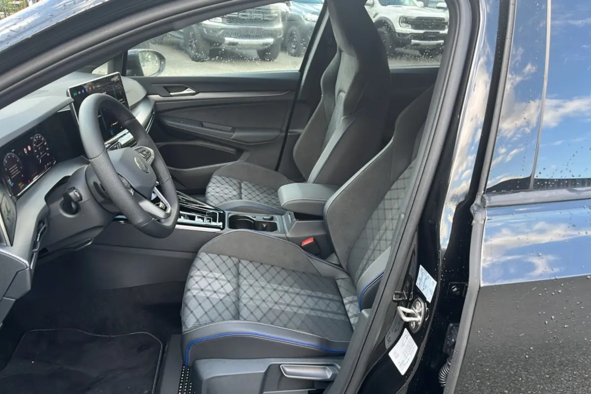 Vue intérieure côté conducteur de la Volkswagen Golf E-TSI 150 R-Line 2026, sièges tissu gris à surpiqûres bleues.