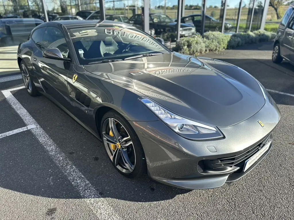 Ferrari GTC4 Lusso gris foncé vue 3/4 avant droit, avec jantes sport et logo cheval cabré sur aile.