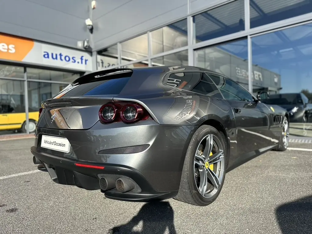 Ferrari GTC4 Lusso gris foncé vue 3/4 arrière droit, avec feux ronds et jantes à cinq branches jaunes.