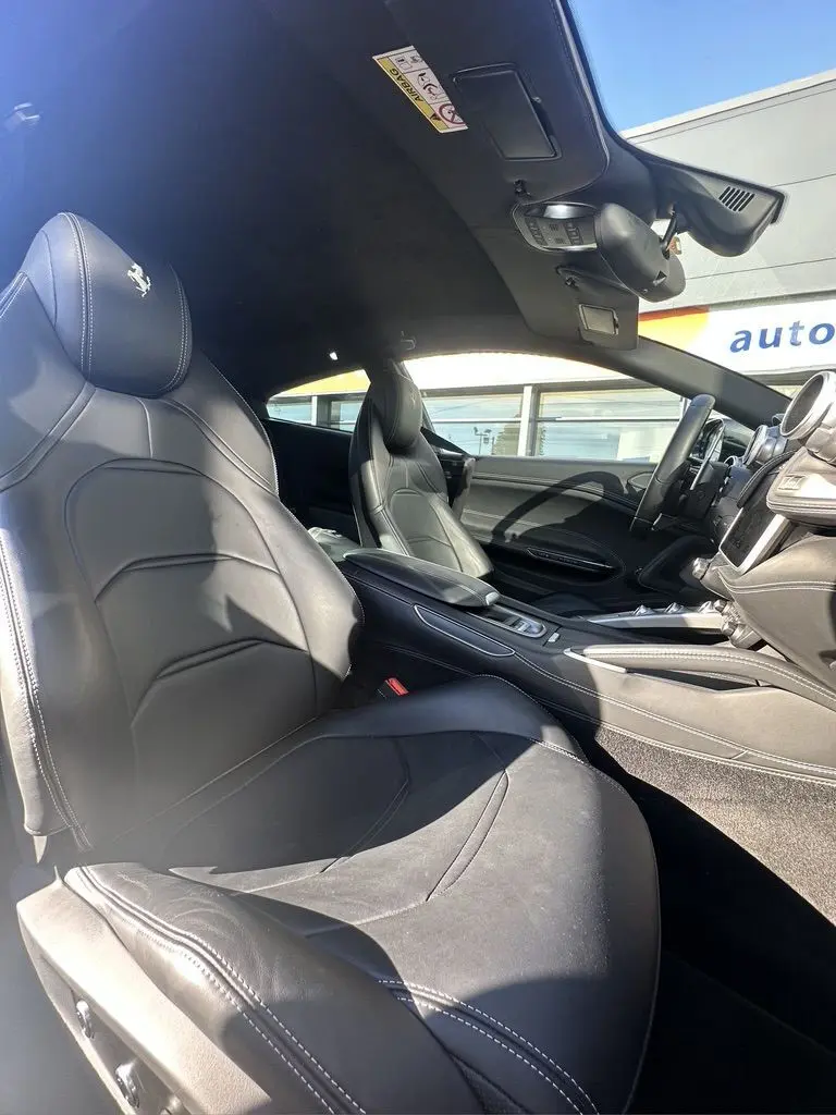 Vue intérieure côté conducteur de la Ferrari GTC4 Lusso 2017 avec sièges en cuir noir et logo cheval cabré brodé.