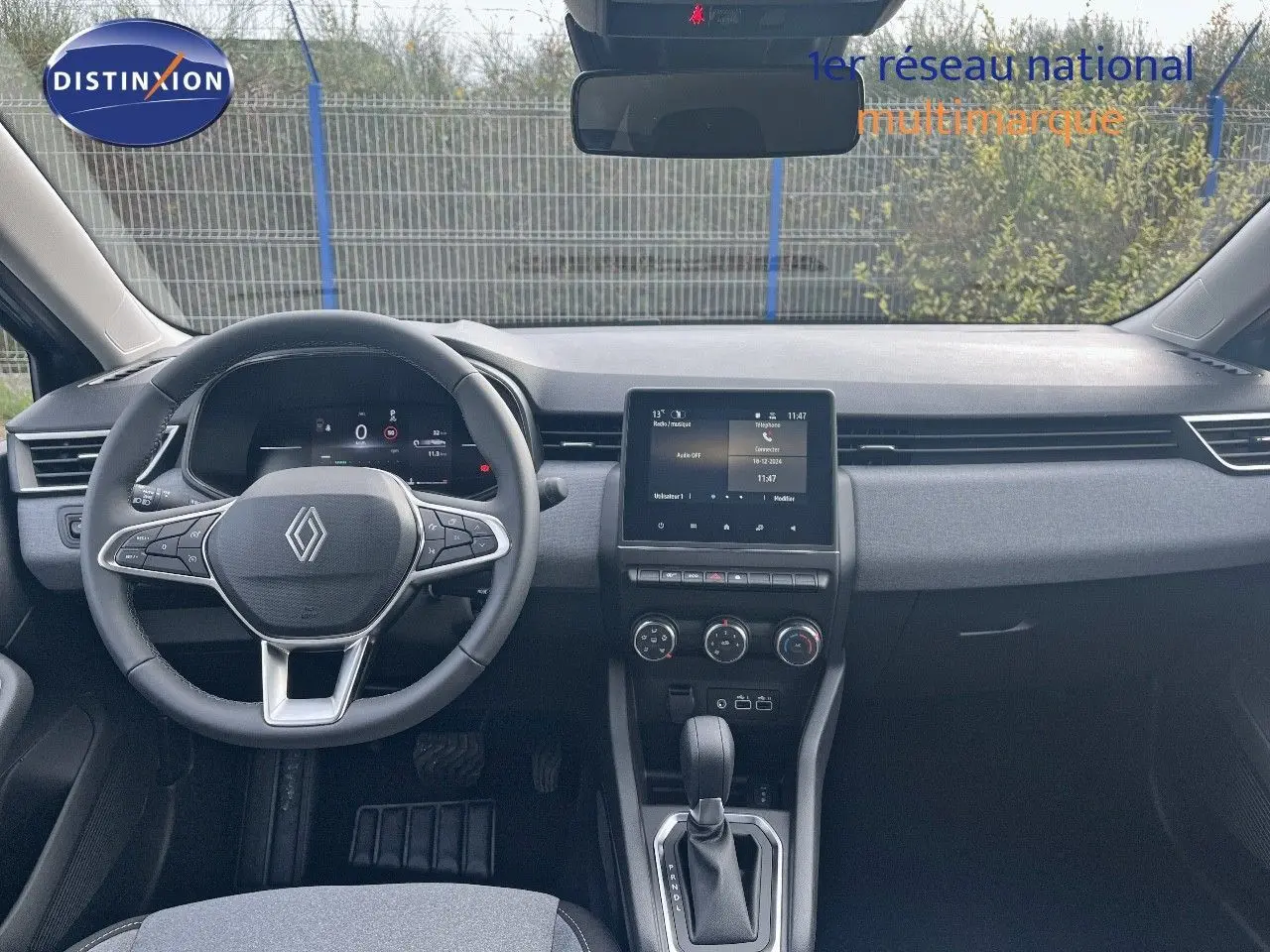 Vue intérieure frontale du tableau de bord et volant de la Renault Clio gris schiste métal 2024 avec écran tactile central et boîte auto.