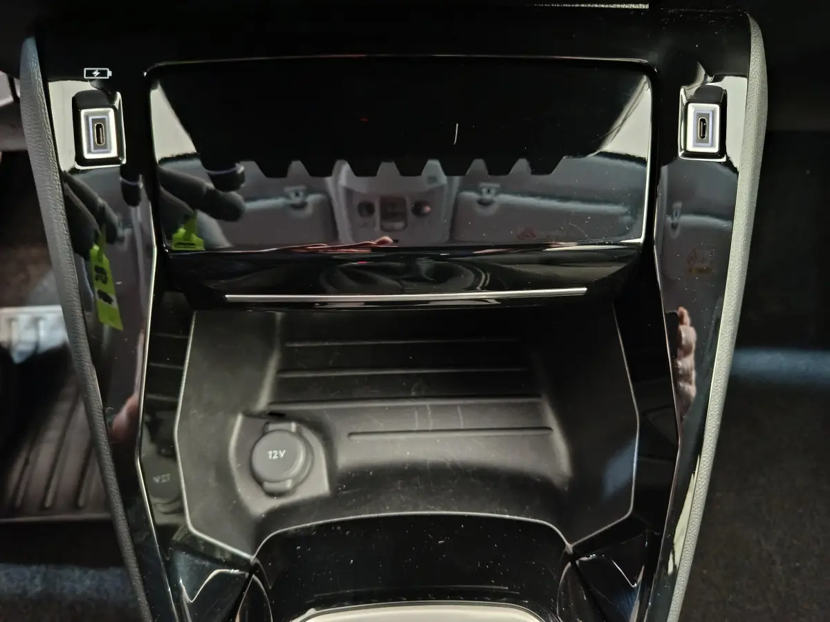 Gros plan sur la console centrale noire brillante de la Peugeot 208 PureTech 100 S&S Allure avec prise 12V visible