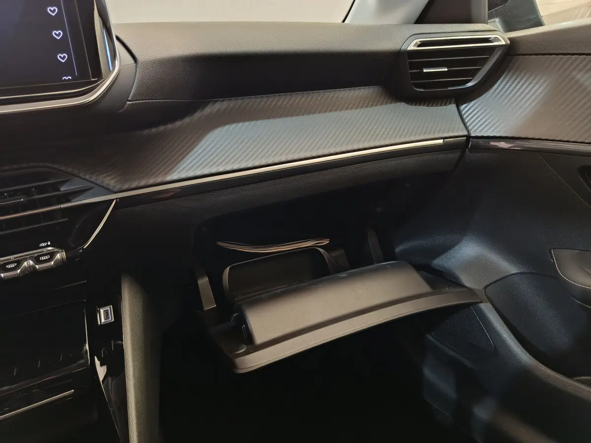 Intérieur de la Peugeot 208 PureTech 100 S&S Allure 2025, vue du tableau de bord côté passager avec boîte à gants ouverte.