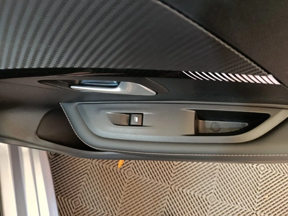 Poignée de porte intérieure côté gauche avec bouton de lève-vitre sur Peugeot 208 gris clair 2025.