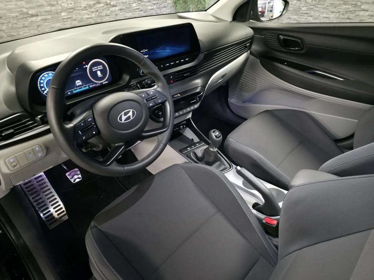 Vue intérieure côté conducteur de la Hyundai Bayon 2025 noire, volant cuir, tableau de bord numérique et levier de vitesses manuel.