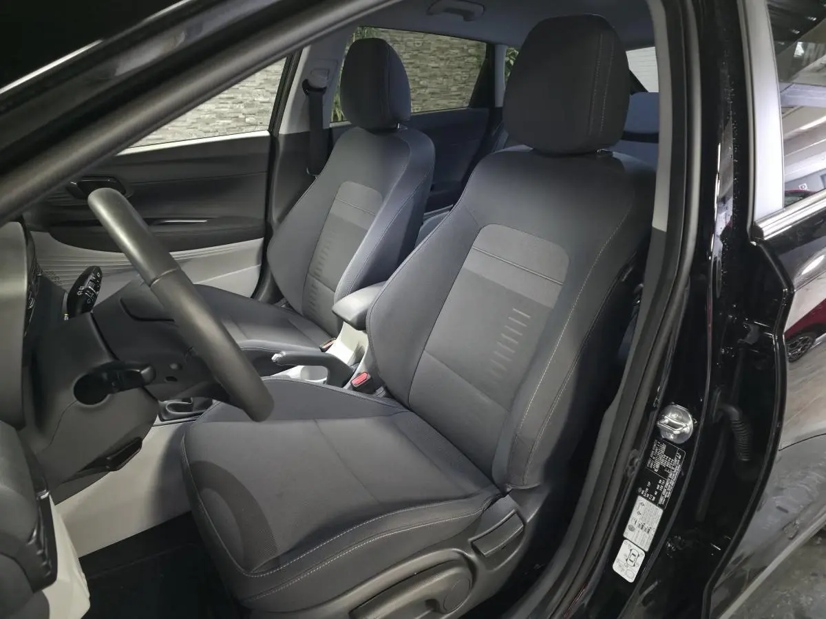 Vue intérieure côté conducteur de la Hyundai Bayon noire 2025, sièges tissu bi-ton gris et noir, volant cuir.