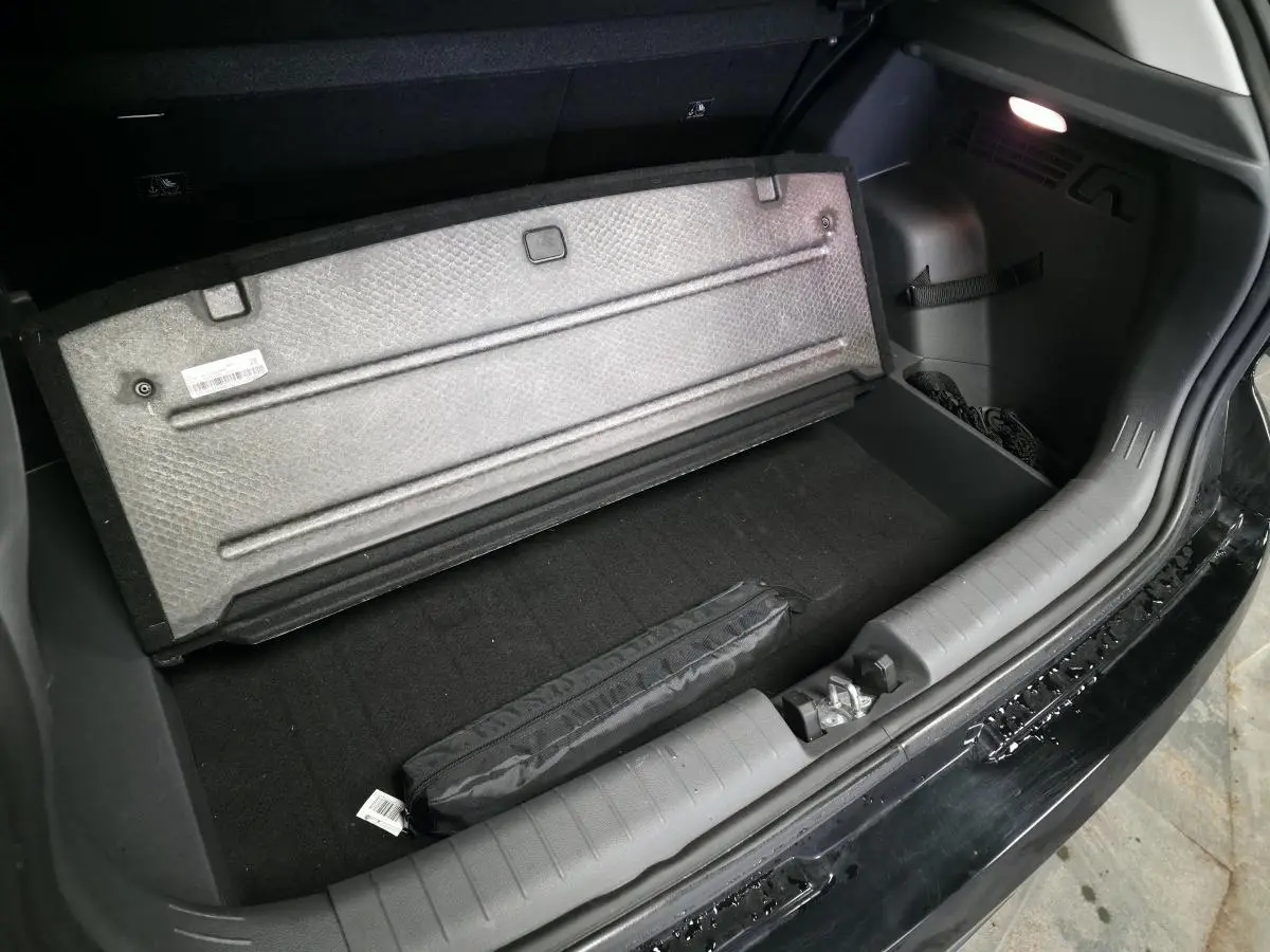 Coffre ouvert d'une Hyundai Bayon noire, vue plongeante sur le plancher et le cache de rangement relevé avec éclairage intérieur allumé.