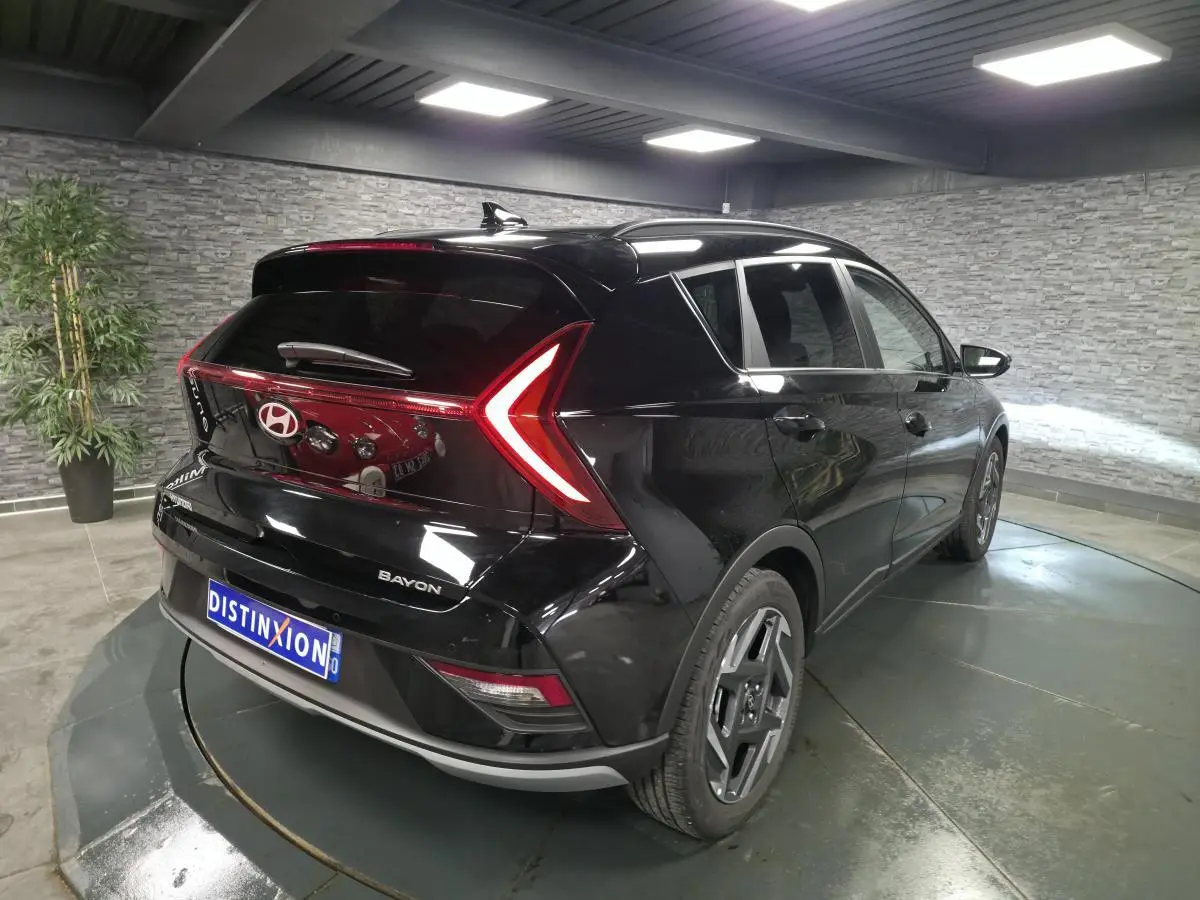 Vue 3/4 arrière droite d'une Hyundai Bayon noire métallisée avec feux arrière LED en forme de V et jantes alliage 17 pouces.