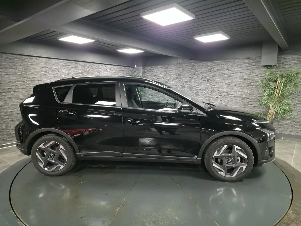 Vue de profil côté gauche d'une Hyundai Bayon 2025 noire métallisée avec jantes alliage 17 pouces dans un showroom.