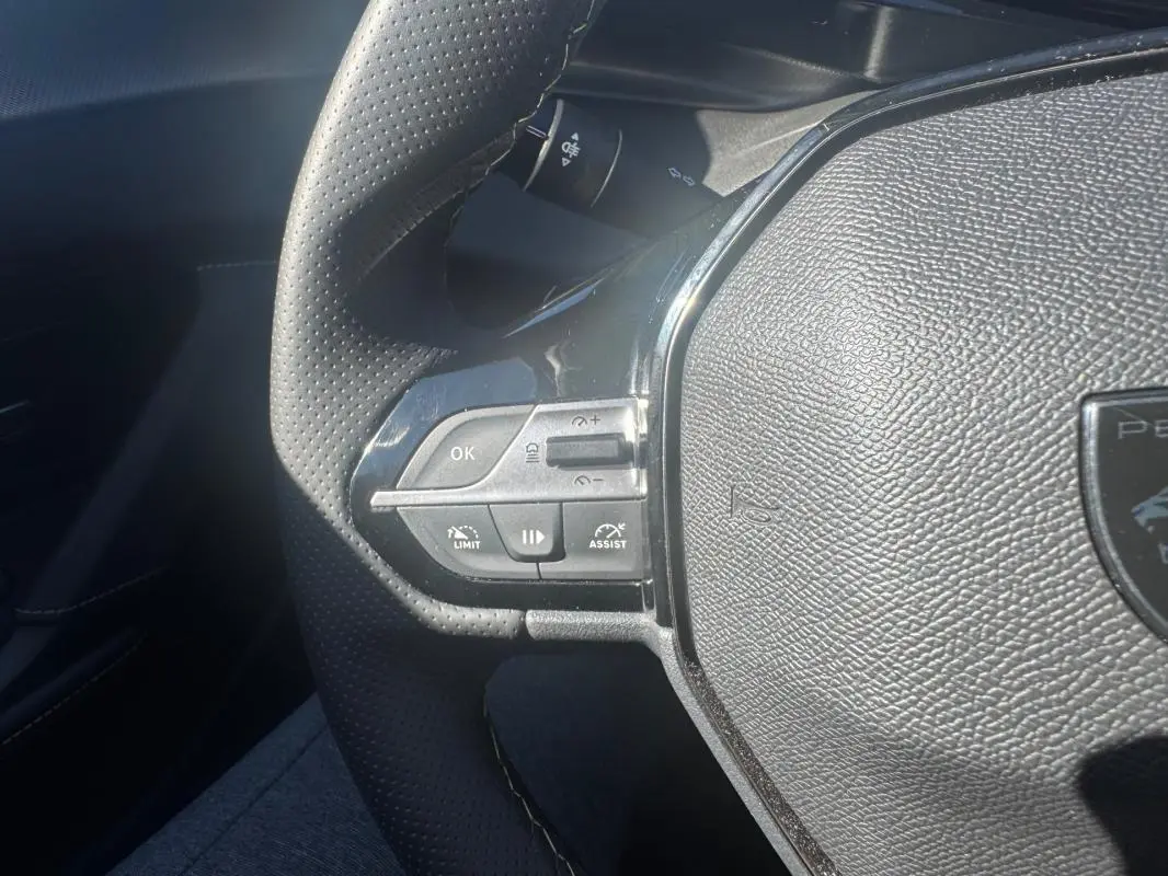 Gros plan sur le volant cuir perforé du Peugeot 408 Hybrid 136 e-DCS6 GT, montrant les commandes intégrées à gauche.
