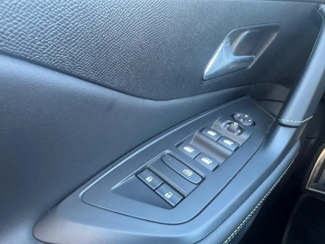 Vue rapprochée de la porte côté gauche de la Peugeot 408 Hybrid gris, montrant les commandes électriques des vitres et rétroviseurs.