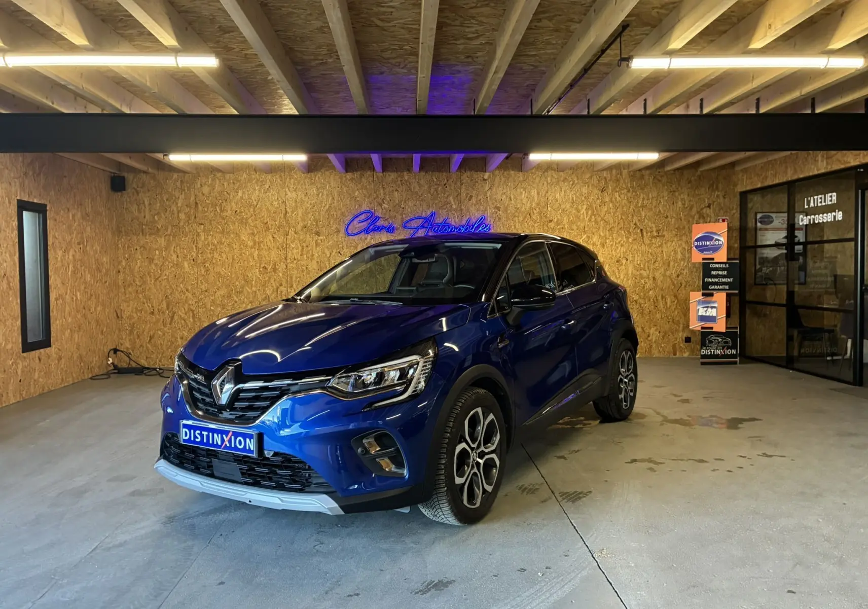 Renault Captur bleu 3/4 avant droit en intérieur, avec calandre chromée et jantes distinctives.