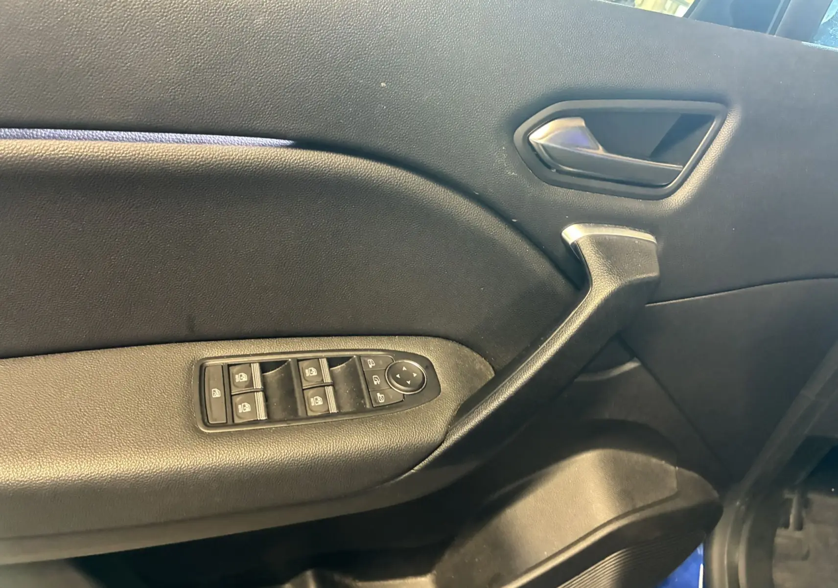 Vue intérieure côté gauche de la porte avant d'un Renault Captur bleu, avec commandes électriques des vitres et poignée noire.